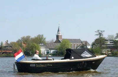 sloep varend op rivier met huizen en bomen op oever