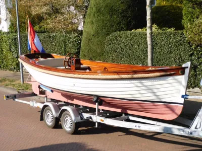 houten sloep op trailer naast haag