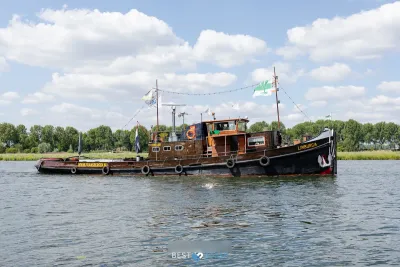 sleepboot op rivier bij boomrijke oever