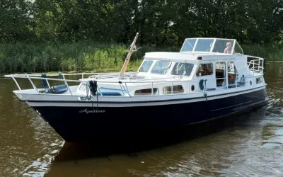 witte motorboot op water langs groene oever