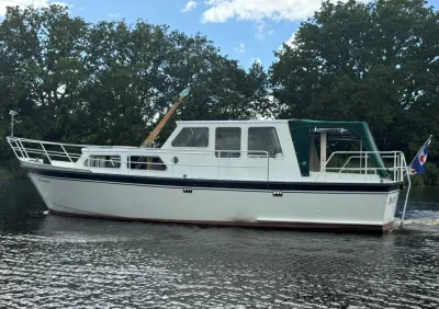 witte kruiser op rustig water met bomen op de oever