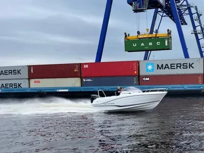 wit open motorjacht op water bij containerkraan
