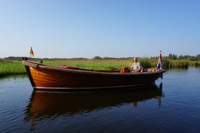 houten sloep met stuurman op rustig water