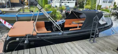 zwarte sloep met zonnedek aangemeerd aan steiger