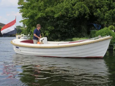 witte sloep op water met persoon en vlag