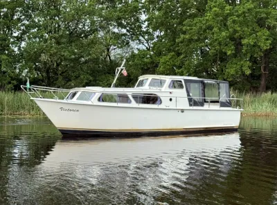 witte kruiser bij riet en bomen op stil water