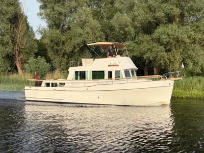 wit motorjacht op rivier met bomen langs oever