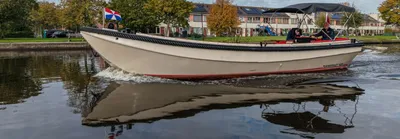 witte sloep op water met huizen op de achtergrond